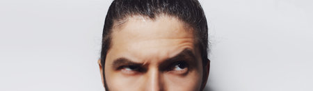 Close-up of male eyes, young man looking up on grey background. Panoramic banner portrait.の写真素材