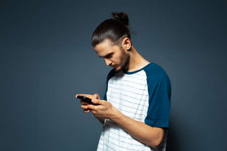 Studio portrait of young attractive man concentrated on his smartphone.