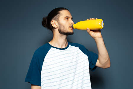 Studio portrait of young attractive guy, drinking water from reusable eco bottle, of yellow colour.の写真素材