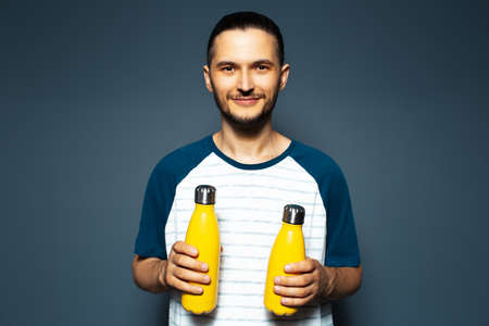 Studio portrait of young smiling guy, with two yellow eco bottles in hands.の写真素材