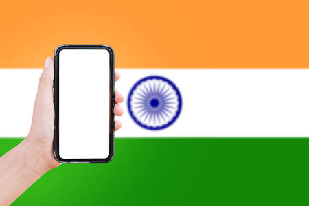 Close-up of male hand holding smartphone with blank on screen, on background of blurred flag of...