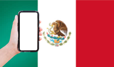 Close-up of male hand holding smartphone with blank on screen, on background of blurred flag of...