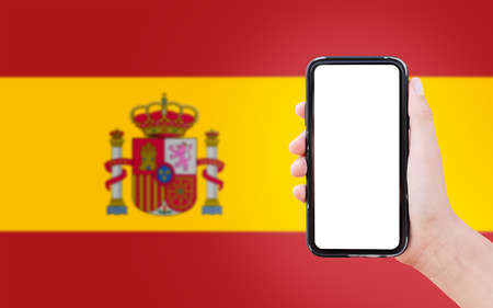Close-up of male hand holding smartphone with blank on screen, on background of blurred flag of...