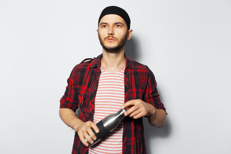 Studio portrait of young handsome man, holding thermo bottle, wearing red plaid shirt and black headband.の写真素材