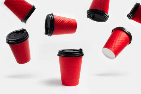 Collage of many paper cups for coffee takeaway of red color with plastic black cap on white background. Pattern concept.の写真素材