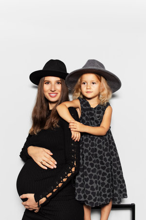 Studio portrait of pregnant smiling woman and child girl, mother and daughter, wearing hats on white background.の写真素材