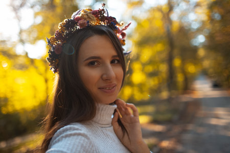 Portrait of young smiling girl with wreath of flowers on head, on background of blurred golden trees in autumn day.の写真素材