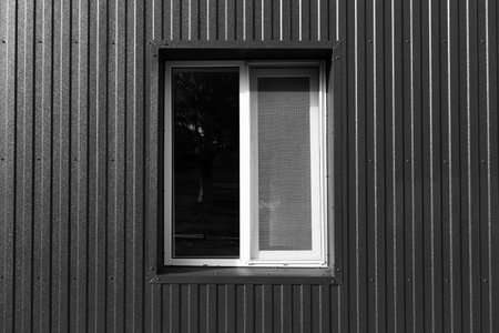 Black and white photo of plastic window of modern barn house with metallic facade.