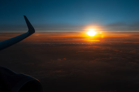 Colorful scenic view of beautiful dark sunset, cloudy sky and airplane wing with engine, through window of the aircraft during the flight. Copy space concept. Silhouette of airliner.の写真素材