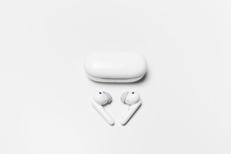 Close-up of wireless earphones lying near charging case on white background.