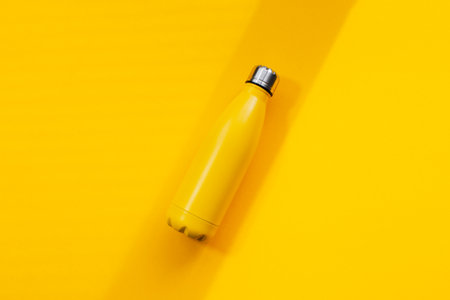 Metal thermo water bottle of yellow color on yellow background. Close-up top view.の写真素材
