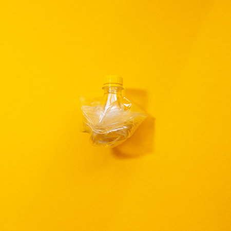 Close-up of crumpled plastic bottle isolated on yellow background.