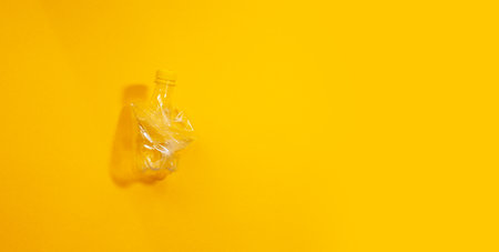 Close-up of crumpled plastic bottle isolated on yellow background with copy space, panoramic banner view.の写真素材