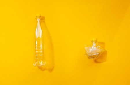 Set of two empty plastic bottles, full and crumpled, collage isolated on yellow background.の写真素材