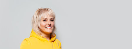 Studio portrait of smiling blonde woman wearing hoodie sweater on white background. Panoramic banner...