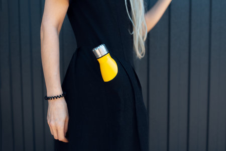 Close-up of young girl in black dress with yellow thermo bottle in pocket.の写真素材