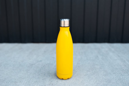 Close-up of steel thermo water bottle of yellow color on the concrete floor against metal background of black color.の写真素材