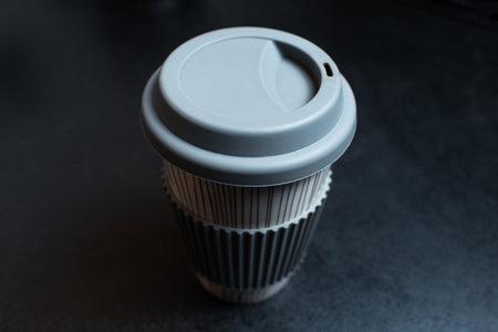 Close-up top view of ceramic cup for coffee takeaway on black background.