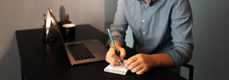 Business panoramic banner view. Young businessman working home at laptop, makes notes in notebook...