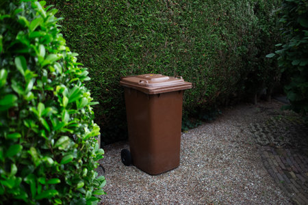 Brown large plastic bin for trash on backyard, around of tree hedge.の写真素材