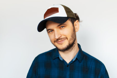 Studio portrait of young man in blue shirt wearing cap, on white background.