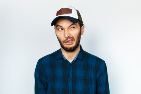 Studio portrait of young man makes funny face, weird expression, on background of white.