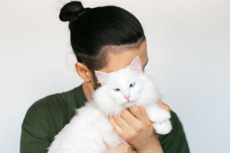Portrait of young man hugging white fluffy cat with blue eyes on white background.の写真素材