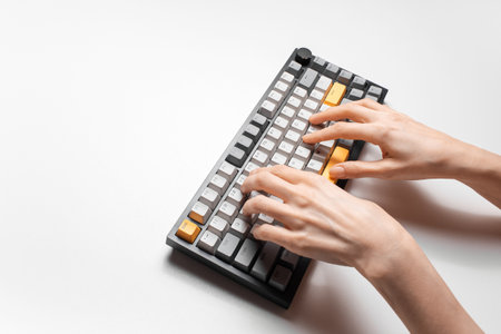 Female hands typing on mechanical keyboard with grey and yellow key cap, on white background.の写真素材