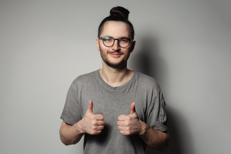 Studio portrait of young man showing thumbs up on grey background.の写真素材