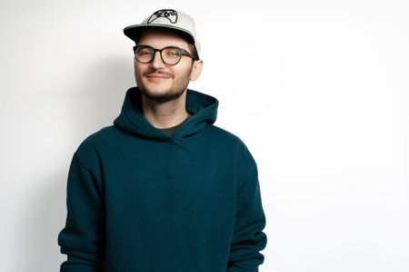 Pleased young guy isolated on white background. Wearing eyeglasses, cap and green hoodie sweater.の写真素材