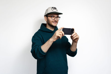 Smiling young man is filming on his smartphone. Isolated on white background.