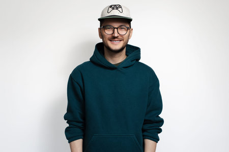 Studio portrait of young man wearing hoodie sweater, eyeglasses and cap.