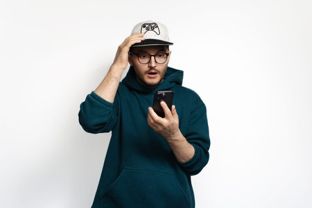 Surprised young man looking in his smartphone with hand on head isolated on white background.