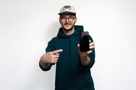 Smiling young man point index finger on smartphone, isolated on white background.