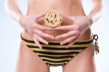 Bottom half of woman wearing swimsuit and holding a cookie in front of her stomachの写真素材