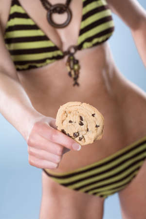 Woman from neck down wearing a swimsuit and holding a cookie away from her bodyの写真素材