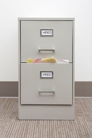 File cabinet labeled Hired and Fired with papers overflowing from the Fired drawer.の写真素材