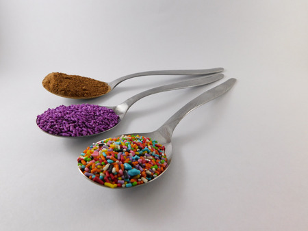 Three spoons with colorful dragees and one with chocolate powder.の写真素材