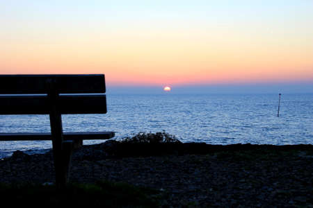 Wooden bench at the ocean at sunriseの写真素材