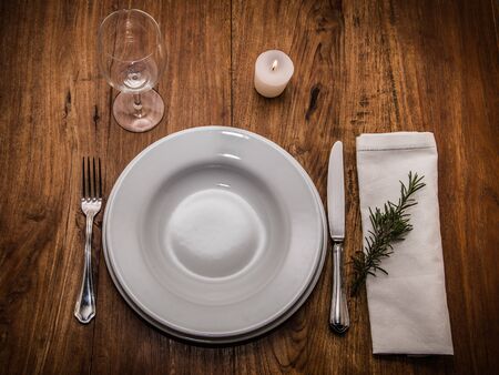 old wooden table set simply with white plates, cutlery, glass, napkin, candle litの写真素材
