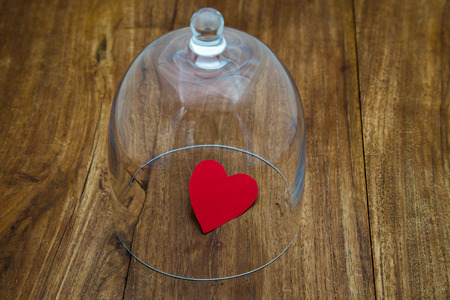 Which glass case protects a small red heart on old wooden tableの写真素材