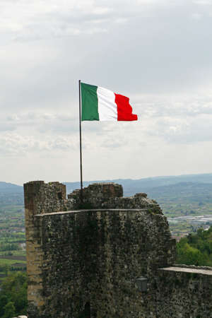 Italian flag flying high above an ancient tower of a castle in Italy の写真素材