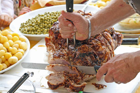 slicing a pork roast with potatoes and peasの写真素材