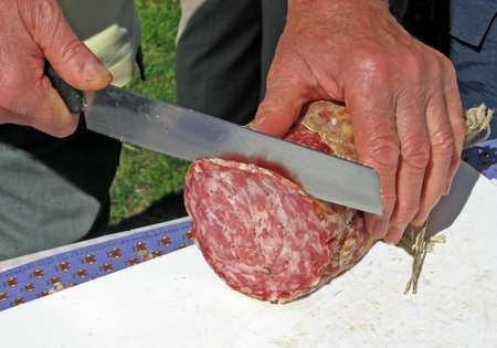 a man cuts a slice of salami with a knife の写真素材