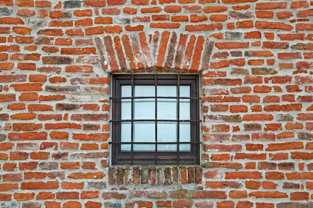 red brick wall with iron lattice window of an ancient prison