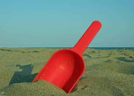 Red toy scoop on the beach by the seaの写真素材