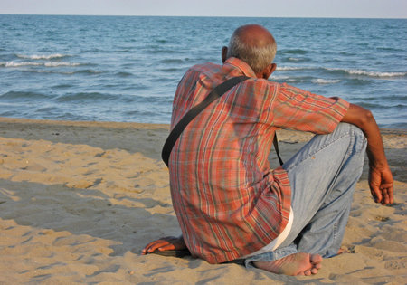 elderly man sitting on the sand waiting on the seashore
