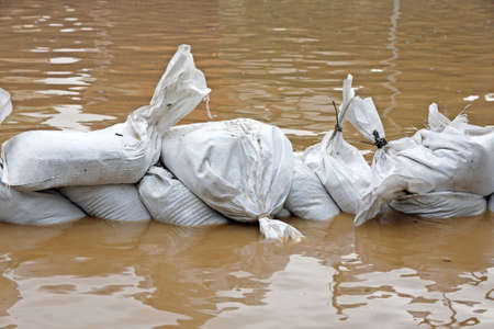White sandbags for flood defense and brown waterの写真素材