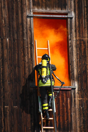 brave firefighters with oxygen cylinder goes into a house through a window during a fire