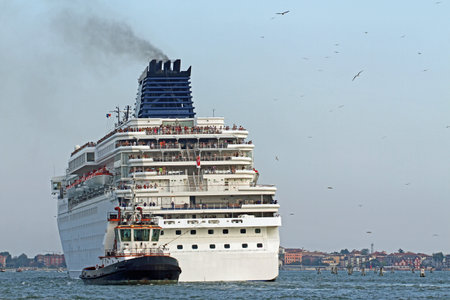 Powerful tugboat while accurately manoeuvre the large cruise ship out of the port city